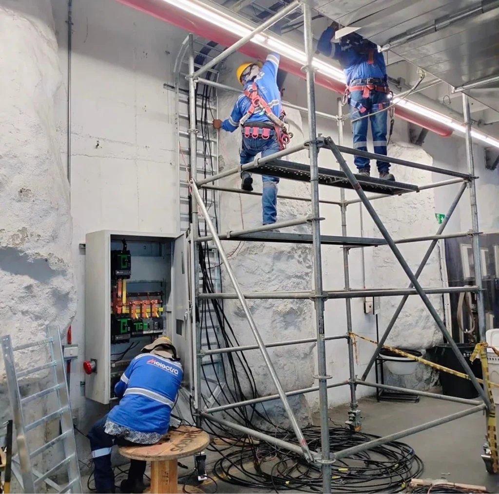 Equipo de técnicos de Melectra realizando el montaje y diseño de infraestructura eléctrica industrial, incluyendo instalación de tableros y cableado en altura con cumplimiento de normas de seguridad.